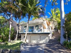 A two-story house with a garage, surrounded by palm trees and a clear blue sky. - Costa Del Sol 4 Park Road 22 (Noosa Heads)