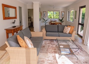 Una sala de estar con un sofá gris, muebles de mimbre y una mesa de centro de vidrio.