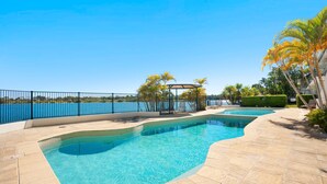 A swimming pool with a curved design, surrounded by a tiled deck and a metal fence.