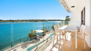 A balcony with a view of a large body of water, a pool, and outdoor seating.