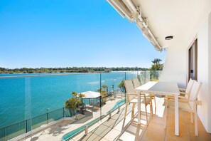 A balcony with a view of a large body of water, a pool, and outdoor seating.