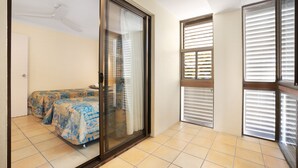 A room with a bed, a sliding glass door, and a window with blinds.