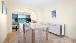 A modern kitchen with a dining area, clear chairs, and a view of the sea.