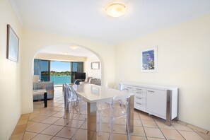 A modern kitchen with a dining area, clear chairs, and a view of the sea.