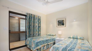 A bedroom with two beds, a sliding glass door, a ceiling fan, and a framed picture on the wall.