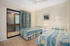 A bedroom with two beds, a sliding glass door, a ceiling fan, and a framed picture on the wall.