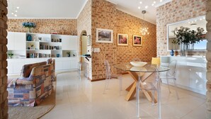 A modern living space with a brick wall, a dining area with a glass table, and a white bookshelf.