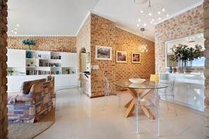 A modern living space with a brick wall, a dining area with a glass table, and a white bookshelf.
