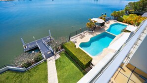 A residential property with a swimming pool, a dock, and a view of a large body of water.