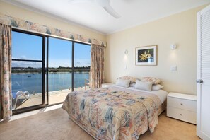 A bedroom with a large bed, a nightstand, a framed picture, and a view of a lake through a sliding glass door. - Aqua Linea 7 Noosa Parade 82 (Noosa Heads)