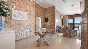 A spacious living area with a brick wall, a glass dining table, and clear chairs.