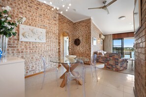 A spacious living area with a brick wall, a glass dining table, and clear chairs.