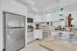 A modern kitchen with stainless steel appliances, white cabinetry, and a granite countertop. - Noosa Views 3 Noosa Drive 33 (Noosa Heads)