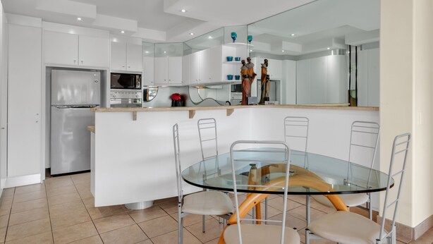 Une cuisine moderne avec des meubles blancs, un four encastré, un four à micro-ondes et une table à manger en verre, accompagnée de chaises.