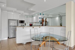 Une cuisine moderne avec des meubles blancs, un four encastré, un four à micro-ondes et une table à manger en verre, accompagnée de chaises.