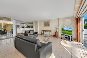 A modern living room with a black leather sofa, a glass coffee table, and a television on a wooden stand. - Noosa Views 3 Noosa Drive 33 (Noosa Heads)
