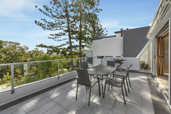 Un balcon avec une table et des chaises, une balustrade et une vue sur les arbres et les bâtiments.