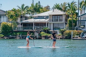 Propiedad frente al agua con una casa, muelle y personas practicando paddleboard.