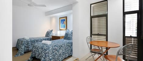 Una camera da letto con due letti, una ventola a soffitto, una finestra con persiane e un tavolino con sedie.