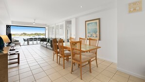 A spacious living area with a dining table and chairs, a sofa, and a view of the sea. - Aqua Linea 3 Noosa Parade 82 (Noosa Heads)