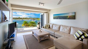 Ein modernes Wohnzimmer mit Sofa, Couchtisch und Fernseher mit Blick auf eine Marina, wo Boote und Palmen zu sehen sind.