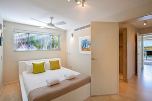 Ein Hotelzimmer mit einem Bett, einem Deckenventilator, einem Fenster mit Jalousien, einer Tür und einem Bild an der Wand.