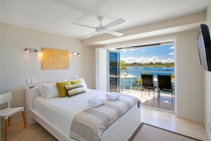 Ein Schlafzimmer mit einem Bett, einem Deckenventilator, Meerblick und einem Balkon mit Stühlen.