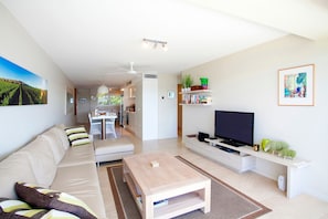 Ein modernes Wohnzimmer mit einer Couch, einem Couchtisch, einem Fernseher und einem Essbereich im Hintergrund.