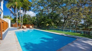 Une piscine dont le bord est recouvert de carrelage, entourée de palmiers et délimitée par une clôture en bois.