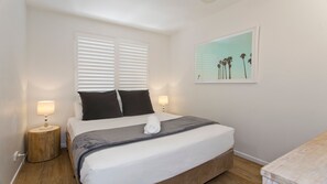 Una camera da letto con un letto, due abat-jour, un quadro appeso al muro e un comodino in legno.