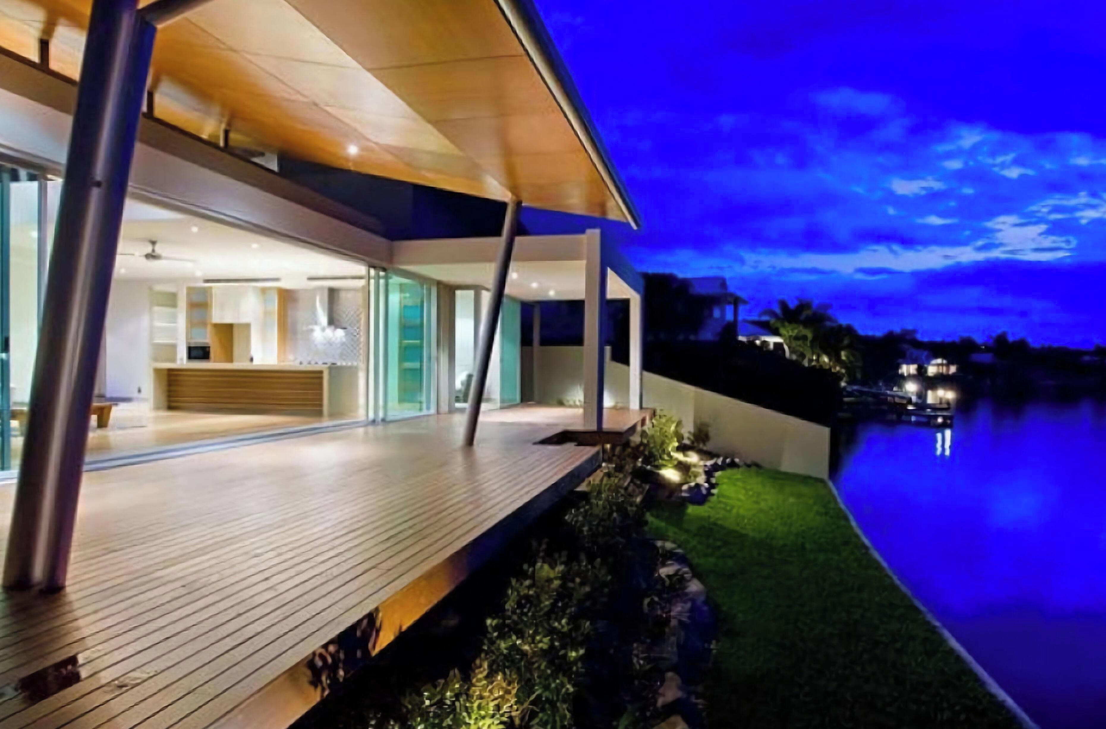 A modern house with a wooden deck and a view of a body of water at night.