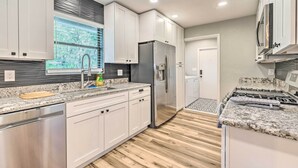 Une cuisine moderne avec des armoires blanches, des appareils en acier inoxydable, un comptoir en granit et un plancher en bois.