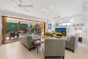 A modern living room with a sofa, armchairs, a coffee table, a TV, and a dining area with chairs and a table.