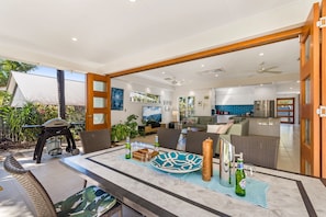 An open-plan living area with a dining table, seating, and a kitchen in the background. - Treasure Cove 6 (Noosaville)