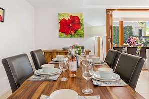 A dining table set with plates, glasses, and a bottle, surrounded by chairs. - Treasure Cove 6 (Noosaville)