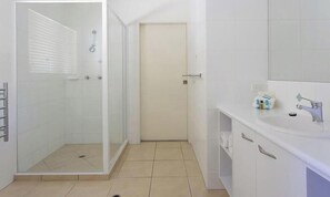 Ein Badezimmer mit Duschkabine aus Glas, einem Waschbecken inklusive Spiegel und einer Tür zu einem weiteren Raum.