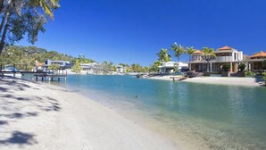 Une plage à l’eau claire, avec un rivage sablonneux et des maisons modernes dotées d’un quai.