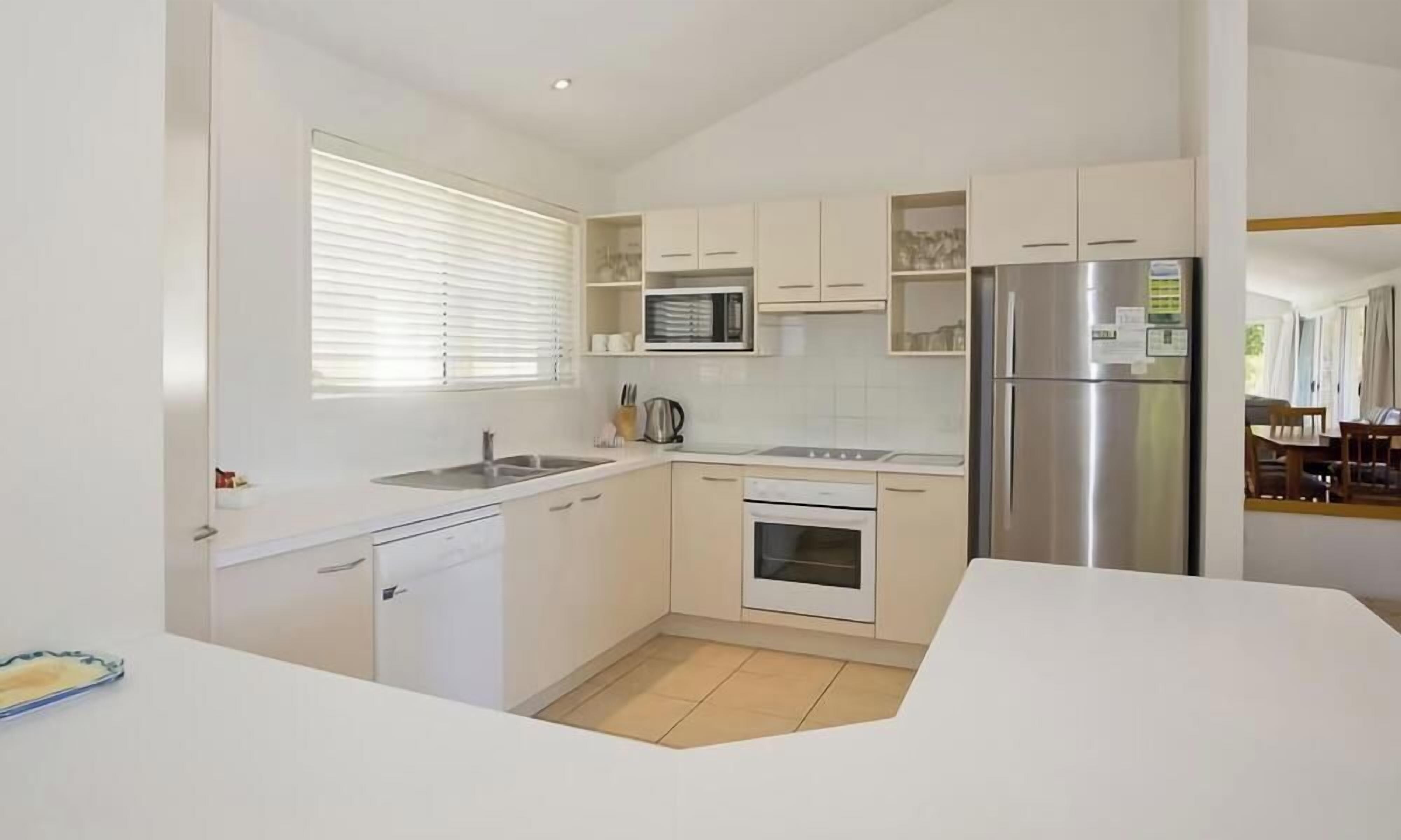 A compact kitchen with white cabinetry, a stainless steel refrigerator, a microwave, and a stove.