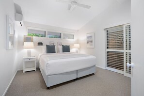 Une chambre à coucher avec un lit, des tables de chevet, un ventilateur de plafond et une fenêtre avec des stores.