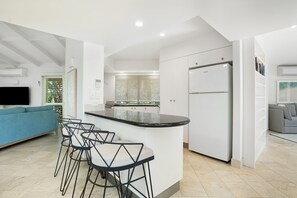 A modern kitchen with a central island, bar stools, a built-in refrigerator, and a TV mounted on the wall. - Witta Circle 24 (Noosa Heads)