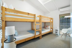 Une chambre avec un lit superposé, un bureau et une chaise, une lampe et une fenêtre avec des stores.