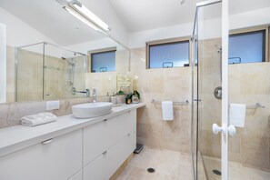 Une salle de bain moderne avec une douche à parois de verre, un grand miroir et un lavabo blanc.