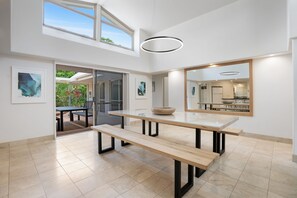 A modern dining area with a glass-top table, benches, and a large mirror reflecting the kitchen. - Witta Circle 24 (Noosa Heads)