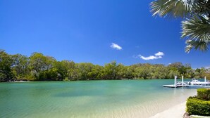 A clear view of a beach with a dock and boats, surrounded by dense greenery. - Wyuna Drive 53 (Noosaville)