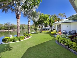 A well-maintained garden with a lawn, palm trees, and a building with outdoor seating.