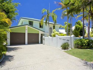 Une maison à deux étages avec un toit végétalisé, une porte de garage marron et une clôture blanche sur laquelle est accroché un panneau.