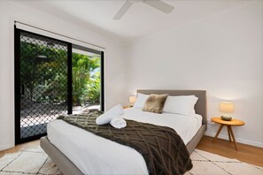 Une chambre à coucher avec un lit, une table de chevet, une lampe et une vue sur l’extérieur, accessible par une porte coulissante.