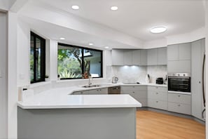 A modern kitchen with a large island, built-in appliances, and a view of greenery outside.