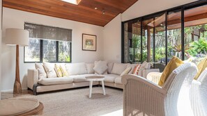 Relax in this spacious living room with a large sofa, round coffee table, and floor lamp, offering a view of lush greenery through the glass doors.
