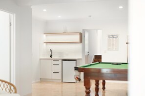 Une pièce avec une table de billard, une petite kitchenette et une porte donnant sur une autre pièce.
